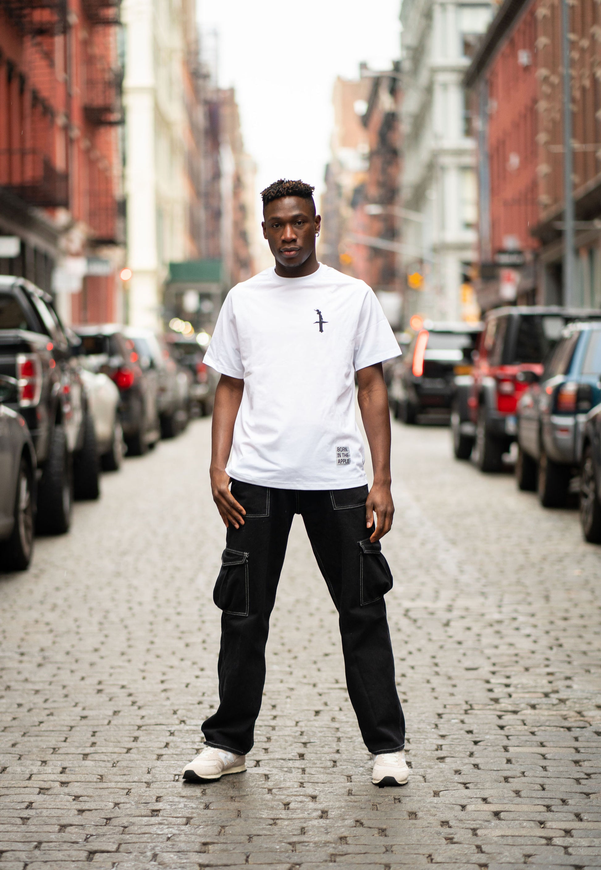 Oversized white t-shirt, heavyweight and 100% cotton. Black embroidered BITA Torch on left chest, grey jock tag with black born in the apple text on bottom left edge, and black screen printed Born In  The Apple text covers the back. Raglan sleeves. 