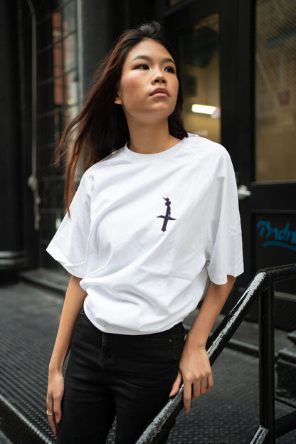 Oversized white t-shirt, heavyweight and 100% cotton. Black embroidered BITA Torch on left chest, grey jock tag with black born in the apple text on bottom left edge, and black screen printed Born In  The Apple text covers the back. Raglan sleeves. 