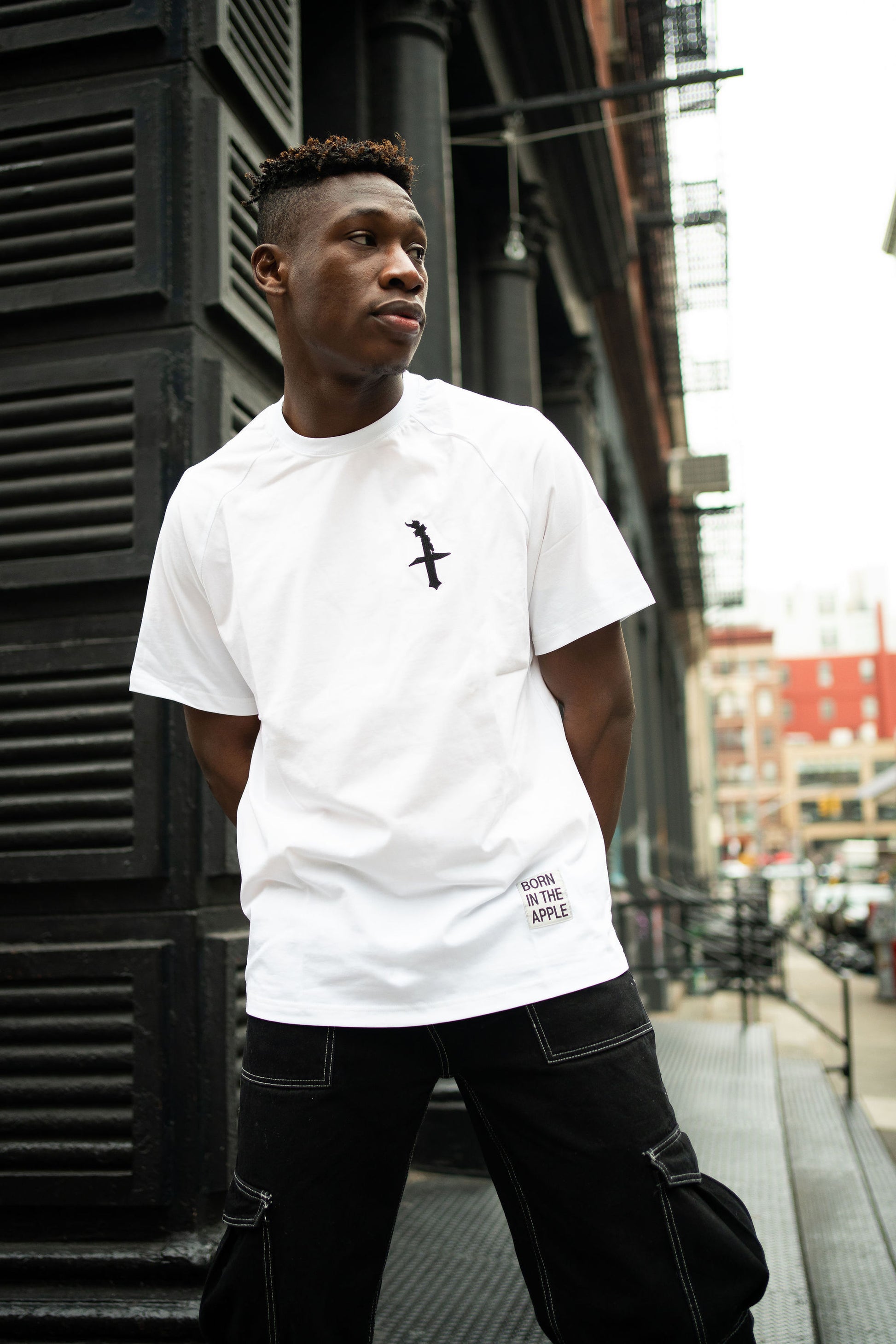 Oversized white t-shirt, heavyweight and 100% cotton. Black embroidered BITA Torch on left chest, grey jock tag with black born in the apple text on bottom left edge, and black screen printed Born In  The Apple text covers the back. Raglan sleeves. 