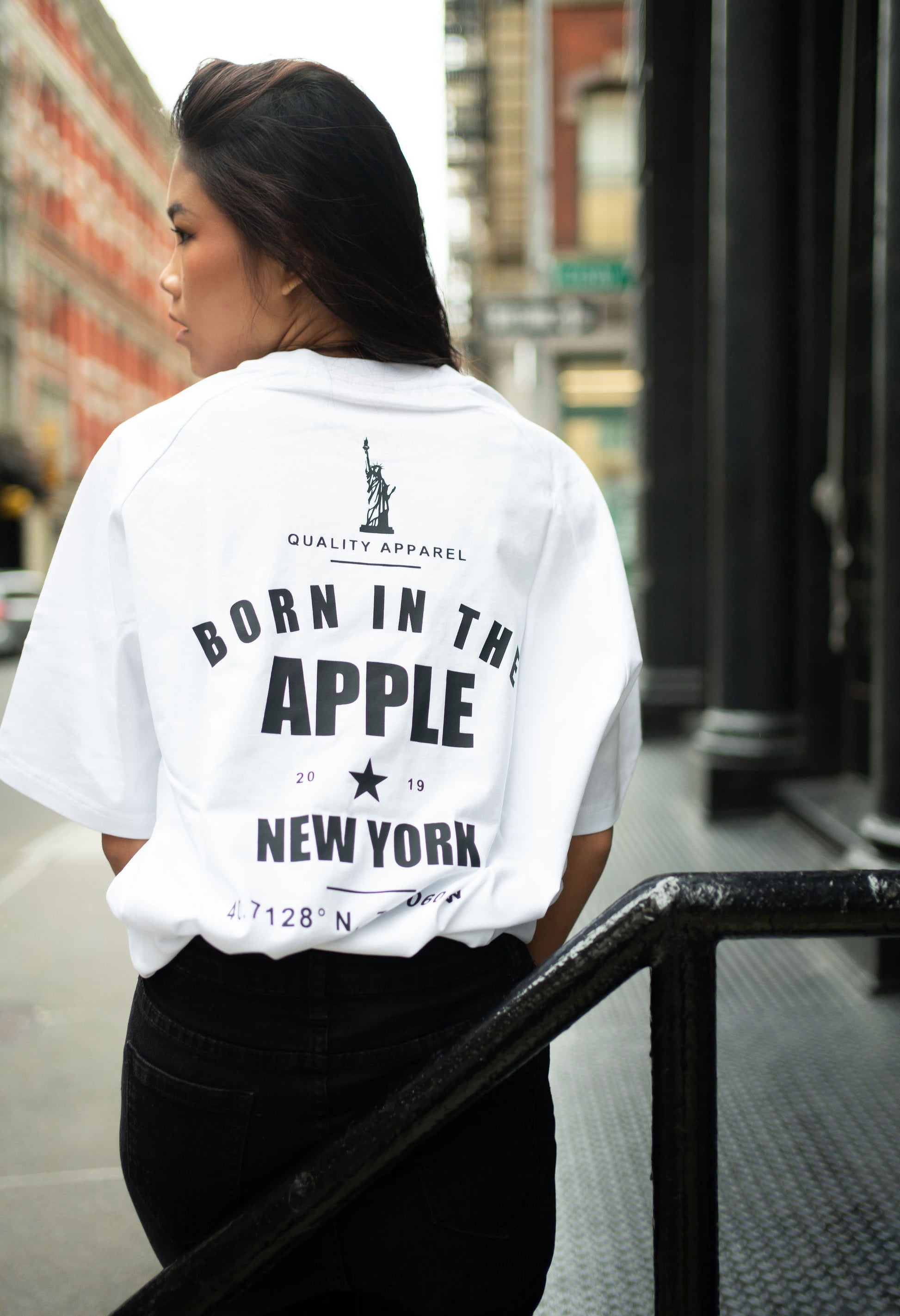 Oversized white t-shirt, heavyweight and 100% cotton. Black embroidered BITA Torch on left chest, grey jock tag with black born in the apple text on bottom left edge, and black screen printed Born In  The Apple text covers the back. Raglan sleeves. 